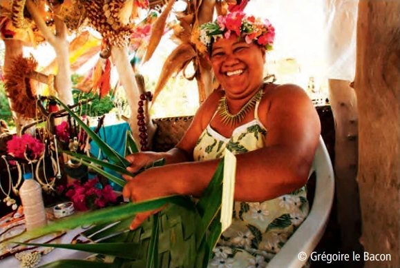 Smiling Polynesian woman with a flower crown on her head, weaving palm leaves.