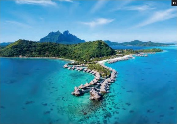 Luftaufnahme des Conrad Bora Bora Nui auf der Insel Toopua mit seinen Overwater-Villen und dem Mount Otemanu im Hintergrund.