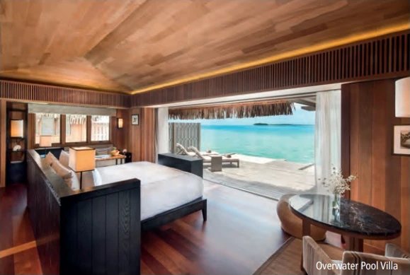 Zimmer einer Overwater Pool Villa mit Bett, Holzdecke und zur Lagune hin offener Terrasse.