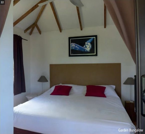 Zimmer eines Garden Bungalows der Havaiki Lodge mit weissem Doppelbett, roten Kissen und Holzdachstuhl.