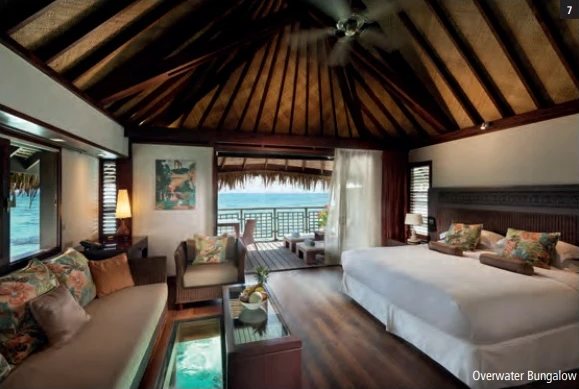 Overwater-Bungalow mit Wohnbereich, Glasboden und Blick von der Terrasse auf die Lagune.