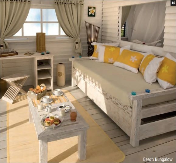 Heller Innenraum eines Beach Bungalows: Tagesbett mit gelben Kissen und ein für das Frühstück gedeckter Salontisch.