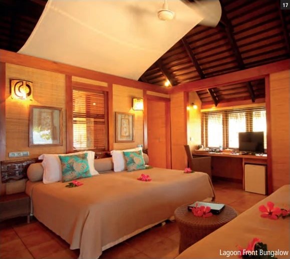 Zimmer im Lagoon Front Bungalow: grosses, mit Hibiskusblüten geschmücktes Bett, Holzdecke und Arbeitsecke.