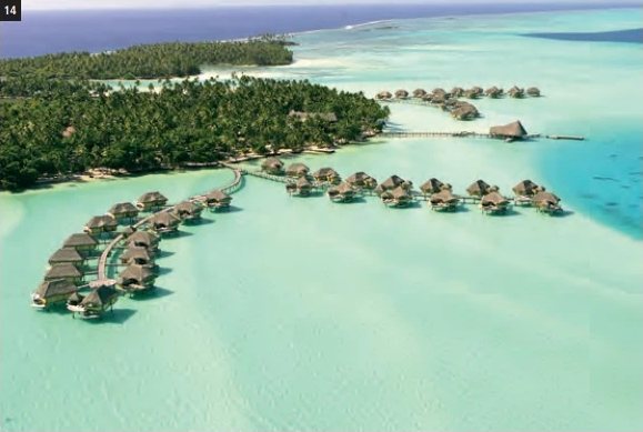 Luftaufnahme des Taha'a by Pearl Resorts mit seinen Overwater-Bungalows in einer türkisfarbenen, von Kokospalmen gesäumten Lagune.