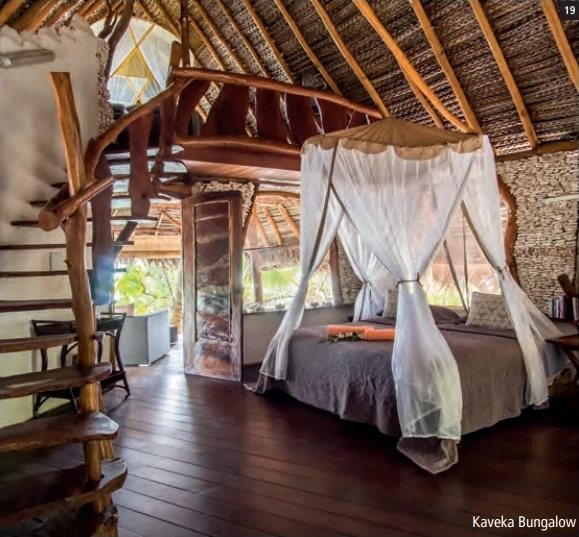 Interieur eines Bungalows mit Dach aus geflochtenen Palmblättern, weiss verhängtem Himmelbett und Treppe aus naturbelassenem Holz.