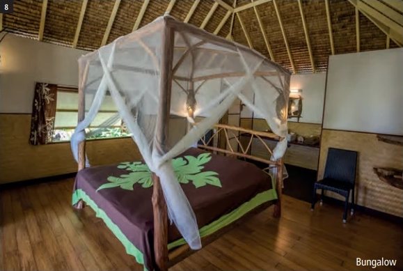 Innenansicht eines Bungalows mit Himmelbett und Moskitonetz, Pandanusdach und Holzparkett.