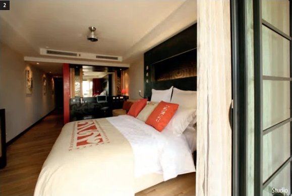 Studio im Te Moana Tahiti Resort mit grossem Bett, orangefarbenen Kissen und Kochnische im Hintergrund.