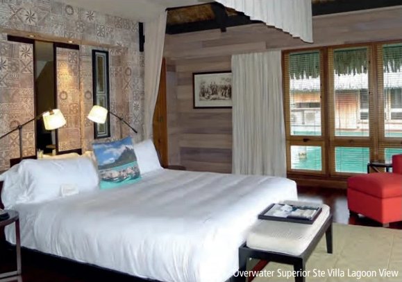 Zimmer einer Overwater-Villa des St. Regis mit grossem weissem Bett und Fensterfront mit Blick auf die Lagune.