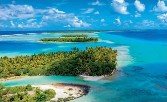 Aerial view of islets covered in coconut palms in a turquoise lagoon with crystal-clear water.