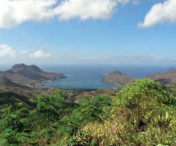 Blick von tropisch bewachsenen Anhöhen auf eine von Bergen umgebene Bucht auf den Marquesas.